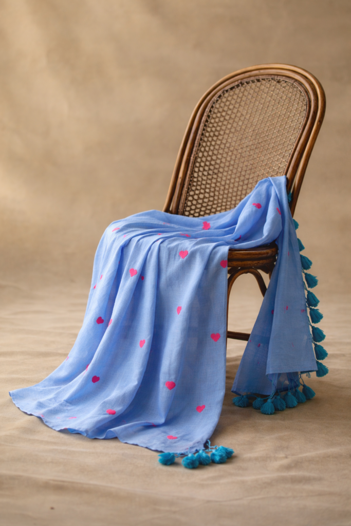 Sky blue linen saree with pink heart motifs draped over wooden chair in aesthetic setup